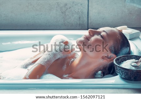 Portrait of a woman with closed eyes of pleasure taking bath at home, female with pleasure enjoys bath with a foam, a day at spa, hygiene and relaxation concept Royalty-Free Stock Photo #1562097121