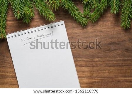 Top view of green spruce twigs with new years resolutions notepad on walnut wood surface