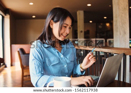 Happy Asian woman in blue shirt holding credit card in hand.