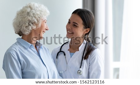 Smiling caring young female nurse doctor caretaker assisting happy senior grandma helping old patient in rehabilitation recovery at medical checkup visit, elder people healthcare homecare concept Royalty-Free Stock Photo #1562123116