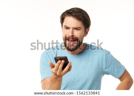 A man in a blue T-shirt looks at the mobile phone, a puzzled look