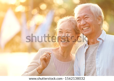 senior asian couple enjoying good time outdoors in park at dusk, happy and smiling Royalty-Free Stock Photo #1562138032