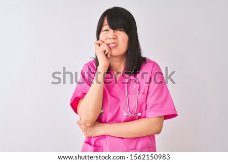 Young beautiful Chinese nurse woman wearing stethoscope over isolated white background looking stressed and nervous with hands on mouth biting nails. Anxiety problem.