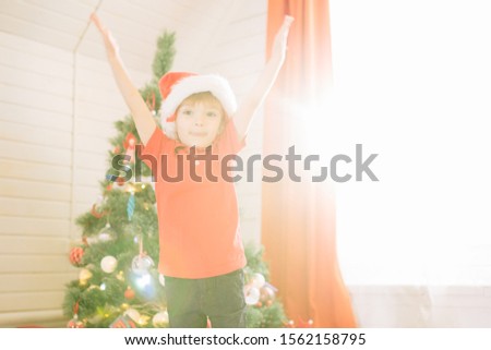 Little cute boy with blue eyes in a Santa Claus hat in a decorated Christmas room with a xmas tree.