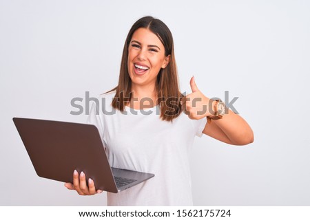 Beautiful young woman working using computer laptop over white background doing happy thumbs up gesture with hand. Approving expression looking at the camera showing success.