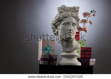 White plaster Statue of Apollo Belvedere, flowers and gifts boxes and packages, spotlights and multi-colored backgrounds. Composition for congratulations, background for design.