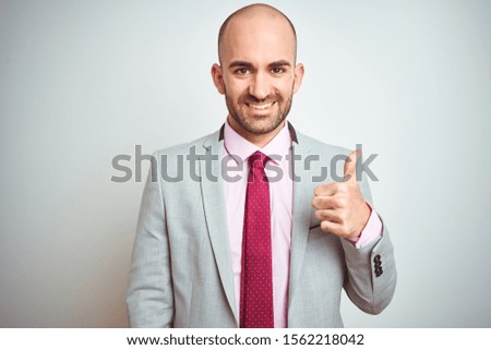 Young business man wearing suit and purple tie over isolated background doing happy thumbs up gesture with hand. Approving expression looking at the camera with showing success.