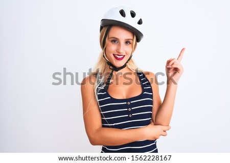Young beautiful woman wearing bike helmet standing over isolated white background with a big smile on face, pointing with hand and finger to the side looking at the camera.