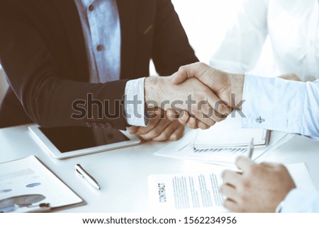Business people shaking hands at meeting or negotiation, close-up. Group of unknown businessmen and women in modern office. Teamwork, partnership and handshake concept, toned picture