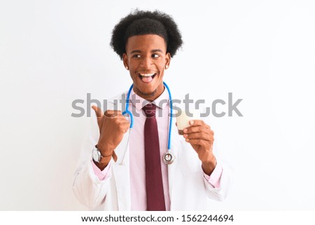 Young african american doctor man drinking glass of milk over isolated white background pointing and showing with thumb up to the side with happy face smiling