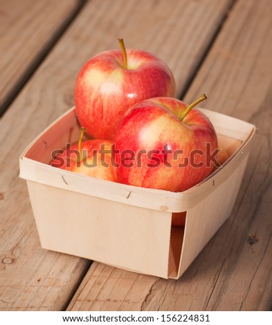 Red and yellow apples in a small woven wood basket on rustic board background