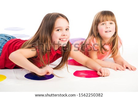 A cute baby in pink clothes lies on stomach on a twister game. Girl smiles and looks up