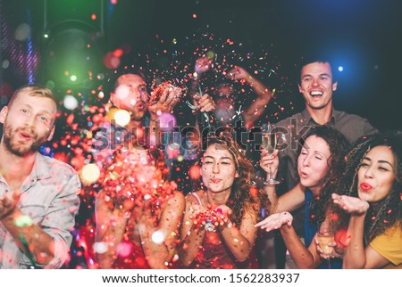 Happy friends doing party throwing confetti in nightclub - Group young people having fun celebrating new year holidays together in disco club - Youth culture entertainment lifestyle concept Royalty-Free Stock Photo #1562283937