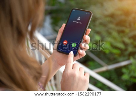 female hands holding phone with incoming call on the screen on the street in the park Royalty-Free Stock Photo #1562290177