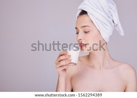 A young girl with beautiful skin in a white towel on her head, after a shower, drinks milk from a glass. Proper nutrition. Lactic acid, lactose. Calcium. Vegetable milk.