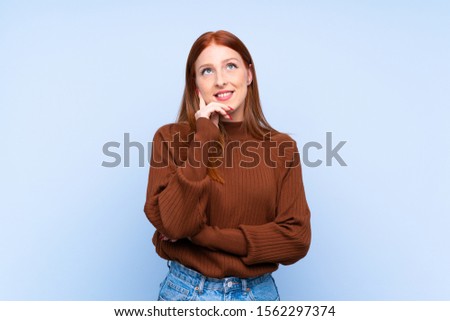 Young redhead woman over isolated blue background thinking an idea while looking up
