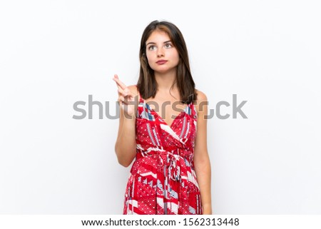 Caucasian girl in red dress over isolated white wall with fingers crossing and wishing the best