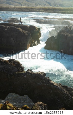 Guy walking on the rocks above the gorge behind Godafoss