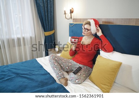 Young woman in red christmas sweater watching TV on the bed