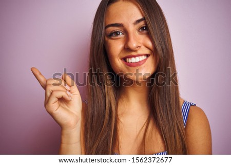 Young beautiful woman wearing t-shirt standing over isolated pink background very happy pointing with hand and finger to the side