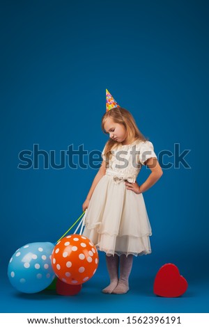 girl in a bad mood with gifts and balloons on the blue background. Studio portrait photos