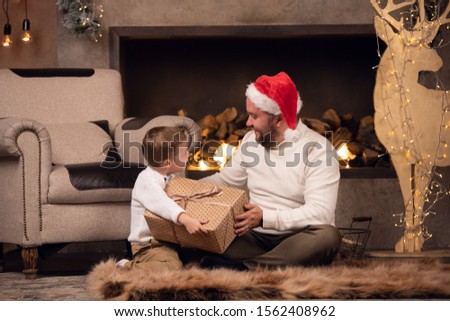 Picture of father in Santa's cap with son sitting on floor on background of fireplace