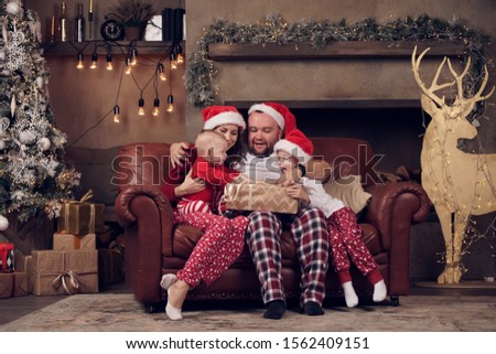 Picture of young parents in Santa's caps and sons on leather sofa in studio near tree