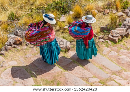 Two Quechua indigenous women in traditional clothing and textile walking down the steps on Taquile island by the Titicaca Lake, Puno, Peru. Royalty-Free Stock Photo #1562420428