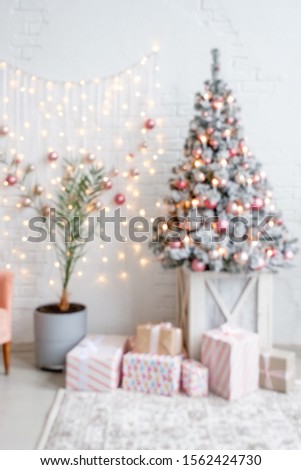 Blurry interior of a light living room with white brick wall a Christmas artificial spruce decorated with lights and balls with gift boxes in wrapping paper. Concept of cozy home christmas decor