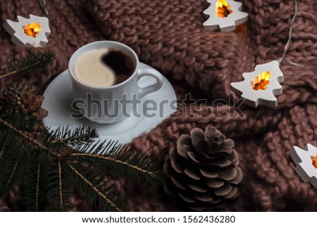 New Year design concept. a white cup of coffee on a brown knitted plaid surrounded by a luminous Christmas tree-shaped garland. cozy christmas atmosphere