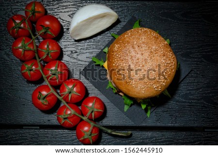 Cheeseburger with mozzarella and branch of cherry tomatos on black tableboard. Ingredients - mozzarella cheese, cherry tomatoes, red onion, arugula, lettuce salad. Fastfood restaurant concept