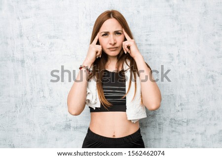 Young fitness woman focused on a task, keeping forefingers pointing head.