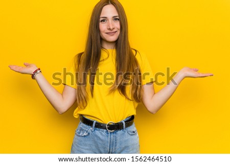 Young ginger redhead woman makes scale with arms, feels happy and confident.