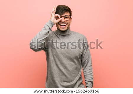 Young smart student man excited keeping ok gesture on eye.