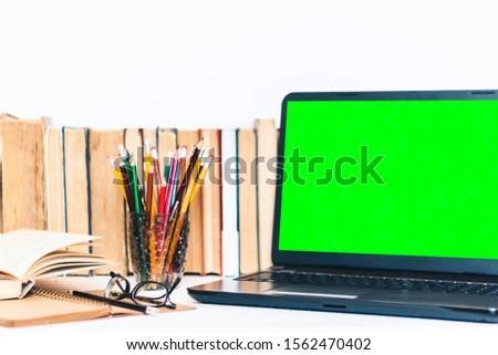 Green screen laptop, pile if books, notebook, smartphone background.Workplace at home during the pandemic. The quarantine concept of stay home stop coronavirus COVID-19 spreading. 