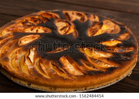 failed apple pie. burnt on top and the dough did not rise during baking. textured burnt pie crust. lies on a wooden table

 Royalty-Free Stock Photo #1562484454