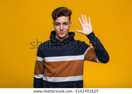 Young cool man wearing a hoodie smiling cheerful showing number five with fingers.