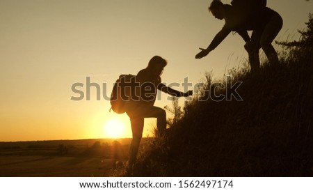 Tourists climb the mountain at sunset, holding hands. teamwork of business people. Traveler man holds out woman's hand to a traveler climbing to the top of the hill. Happy family on vacation.