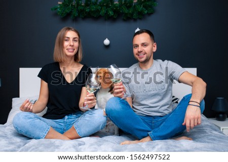Young couple sitting on a bed in the bedroom, hugging. Near them is their dog. Domestic animal Beagle