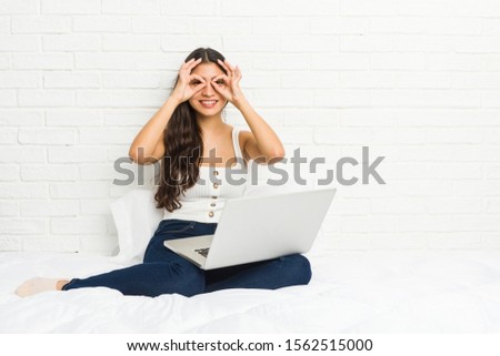 Young arab woman working with her laptop on the bed showing okay sign over eyes