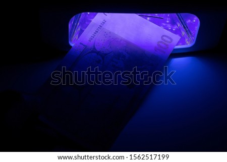 One hundred euro paper bill. Checking money on infrared light at the detector. Check for fake or genuine. Counterfeiting of banknotes, checking at the bank by a cashier of 100 euros.