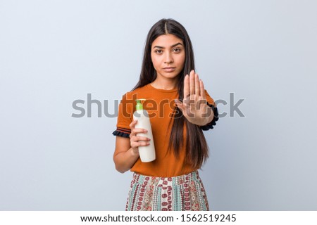 Young arab woman holding a cream bottle standing with outstretched hand showing stop sign, preventing you.