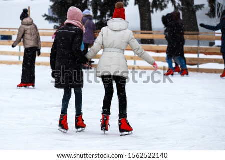 Winter ice rink. The girls in the red skate riding on the ice. Active family sport during the children Christmas winter holidays. School sports clubs. Dnipro city, Dnepropetrovsk, Ukraine