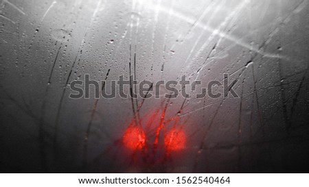 Red lights of a car behind of wet window