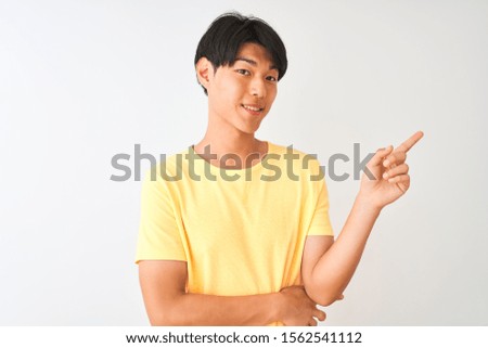 Chinese man wearing yellow casual t-shirt standing over isolated white background with a big smile on face, pointing with hand and finger to the side looking at the camera.