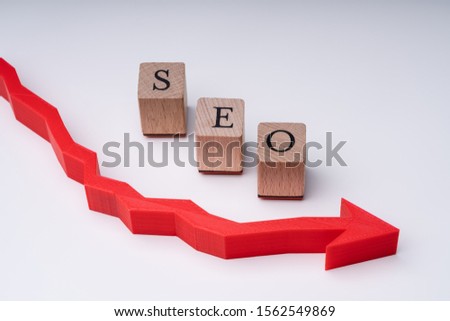 SEO Letters On Wooden Blocks Arranged On Red Decreasing Directional Arrow Against Grey Background