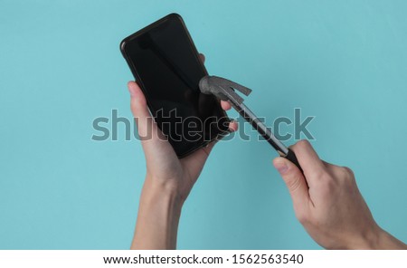 Female hand smashes smartphone screen with hammer on blue background
