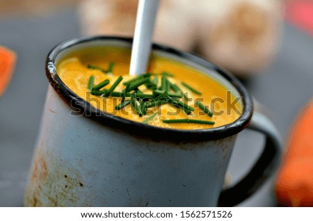 Close-up of pumpkin, carrot soup with cream, fresh chive and spoon in old enamel cup.