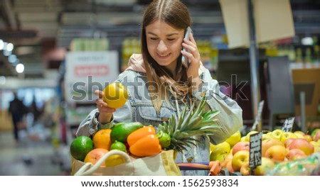 A young woman buys groceries in a supermarket with a phone in her hands. Health food.