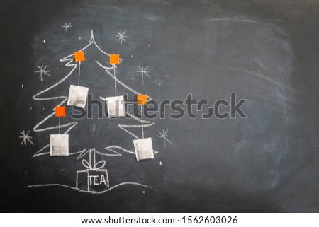 A cup of tea and a Christmas tree decorated with tea bags. Drawing on chalk board.